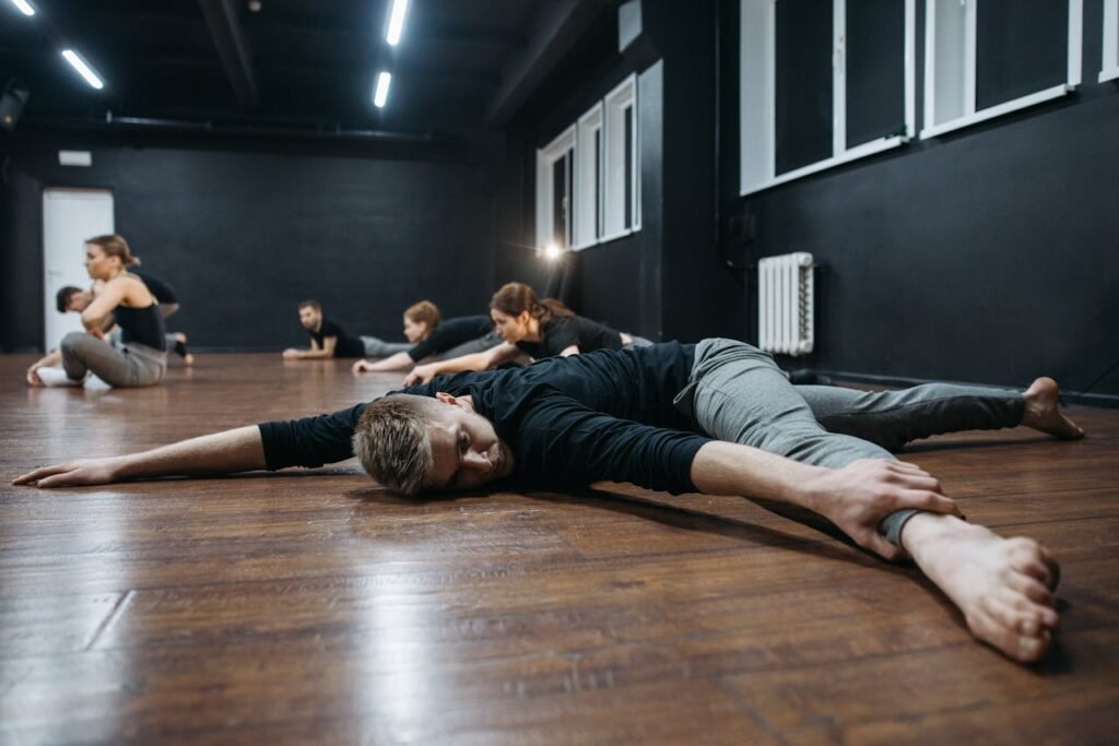 pexels-photo-6926058 A group of adults practicing stretching exercises in a modern dance studio with wooden floors.